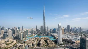 A small white helicopter flies at a distance from Burj Khalifa above Downtown Dubai under a clear blue sky