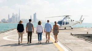 Five people seen from behind walking to a white helicopter on a seaside helipad, Dubai skyline in the distance