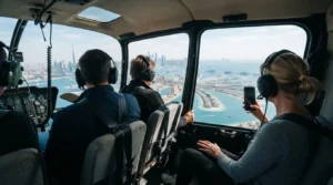 Passengers in headsets seated in a helicopter cabin, one taking a phone photo of the Palm Jumeirah and Dubai skyline
